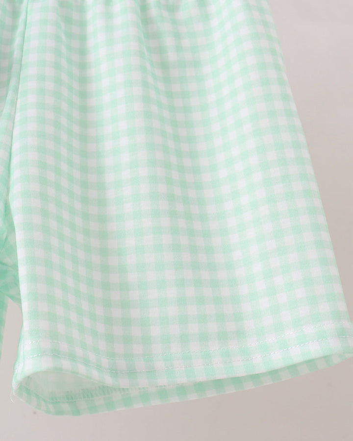 A close-up of a mint green and white gingham checkered fabric, showing the texture and pattern against a light neutral background.