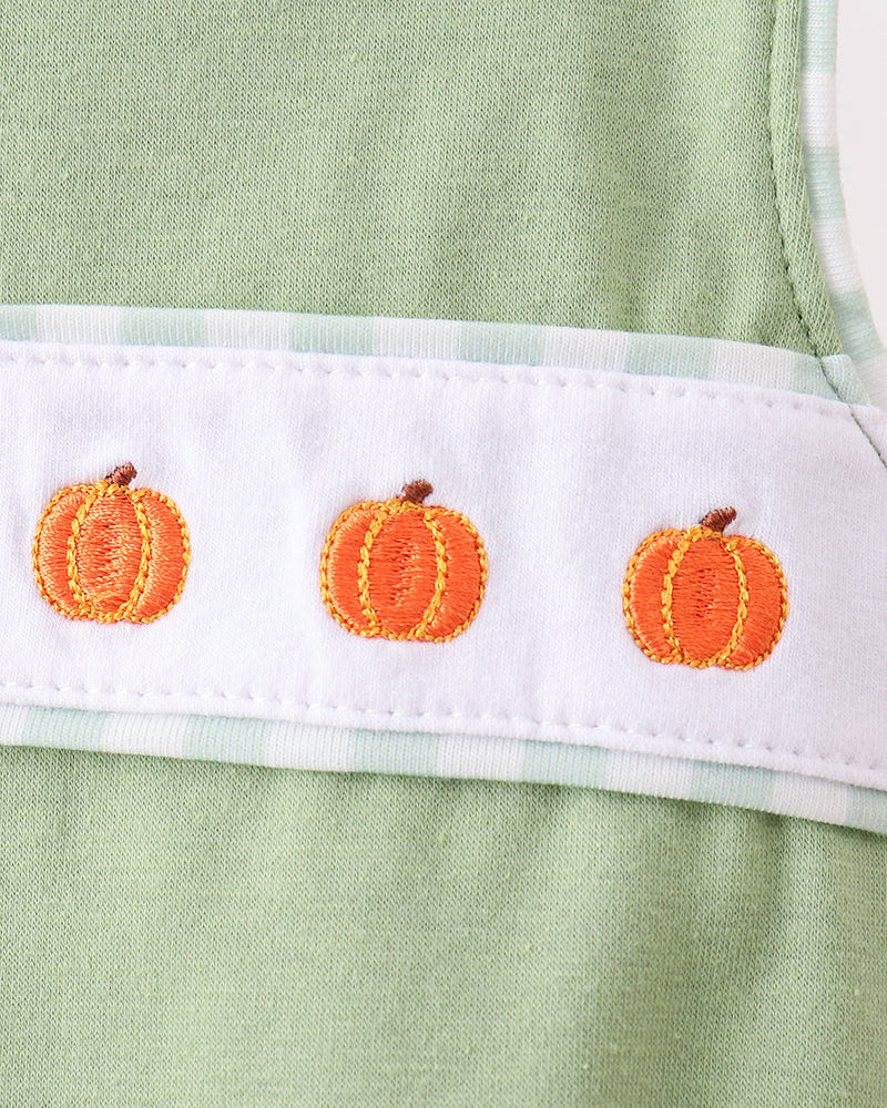 Close-up of a light sage green garment with a white horizontal band featuring three embroidered orange pumpkins.