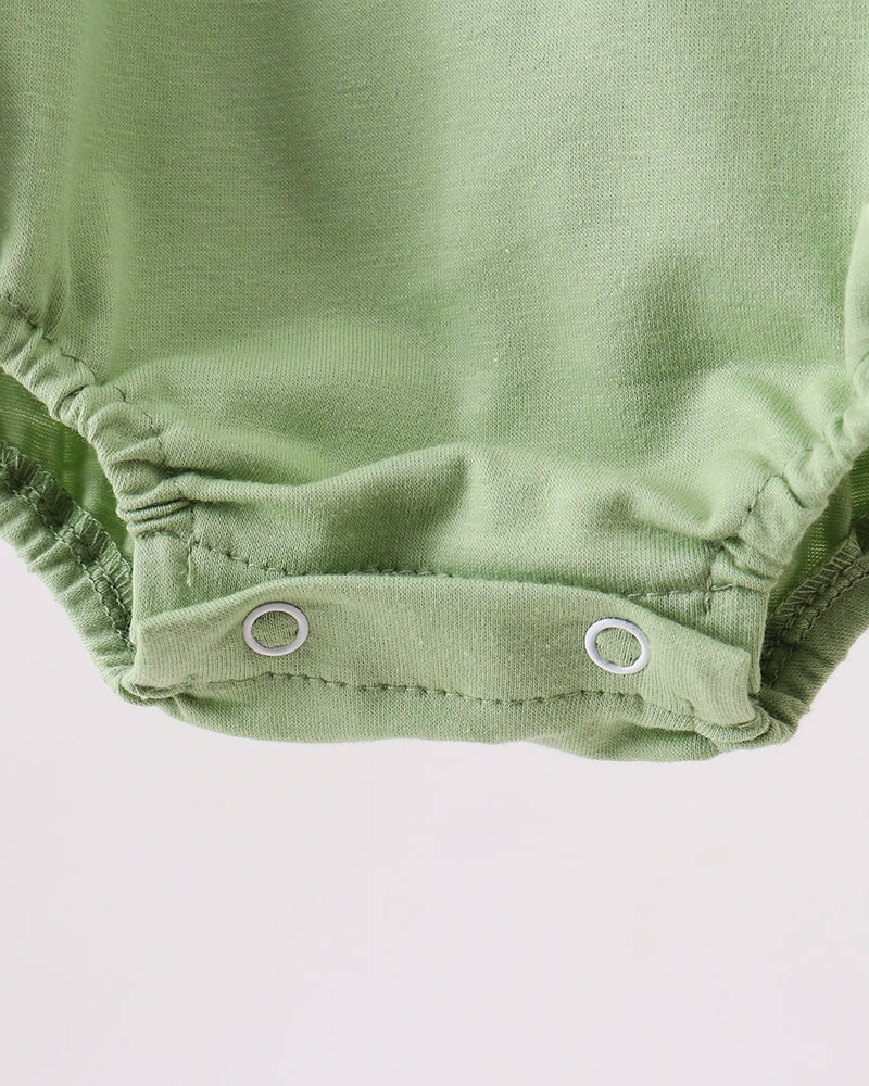 Close-up of a light sage green baby bodysuit showing the snap-closure bottom with two silver metal snaps against a plain light background.