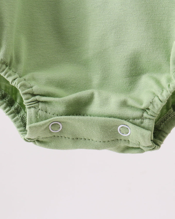 Close-up of a light sage green baby bodysuit showing the snap-closure bottom with two silver metal snaps against a plain light background.