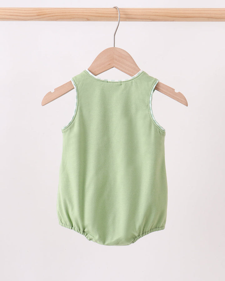 A light sage green sleeveless baby romper with elasticated leg openings, hanging on a wooden hanger from a wooden clothes rack against a plain off-white background.