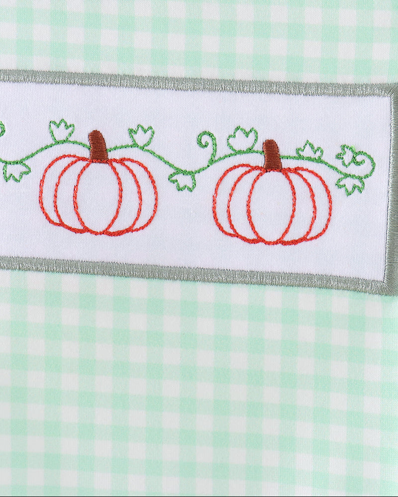 Close-up of a baby shirt featuring a mint green and white gingham pattern, a gray ribbed collar, and an embroidered white chest patch with two red pumpkins and green vines.