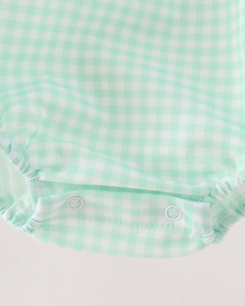 Close-up of a baby romper or bodysuit fabric in a mint green and white gingham check pattern, showing the elastic crotch area with two snap buttons.