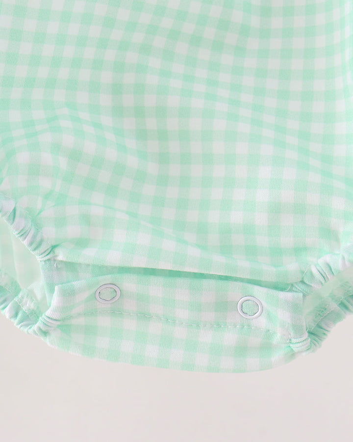 Close-up of a baby romper or bodysuit fabric in a mint green and white gingham check pattern, showing the elastic crotch area with two snap buttons.