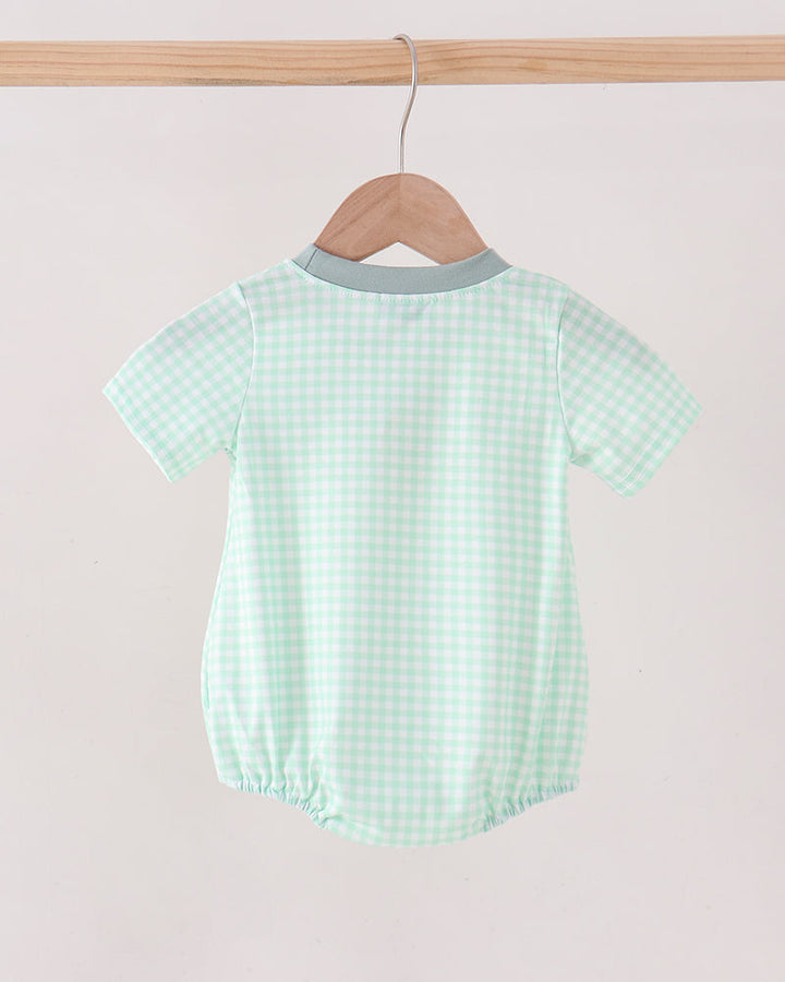 A baby short-sleeve romper in a light mint green and white gingham check pattern, hanging on a wooden hanger from a wooden clothes rack against a plain off-white background.