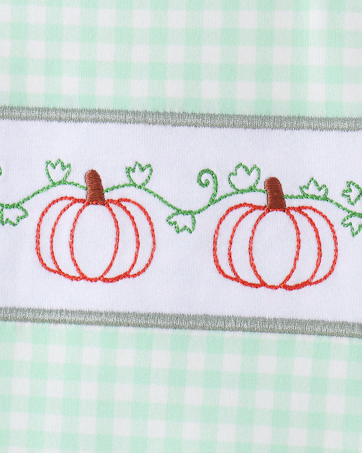 A close-up of a white embroidered band featuring two orange pumpkins with green vines and leaves, bordered by a gray stitched edge, set against a mint green and white gingham background.