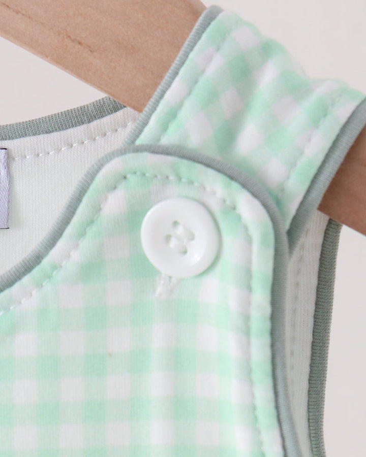 Close-up of a baby garment with a mint green and white gingham pattern, featuring a white snap button closure and ribbed trim.