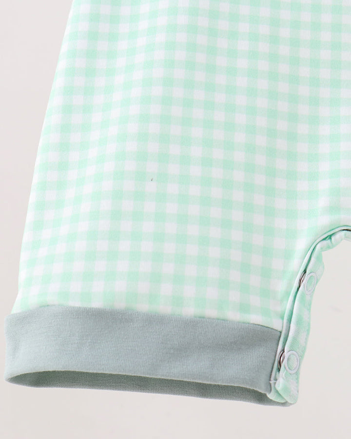 Close-up of a baby garment showing a mint green and white gingham pattern with a solid light sage green cuff and snap-button closure.