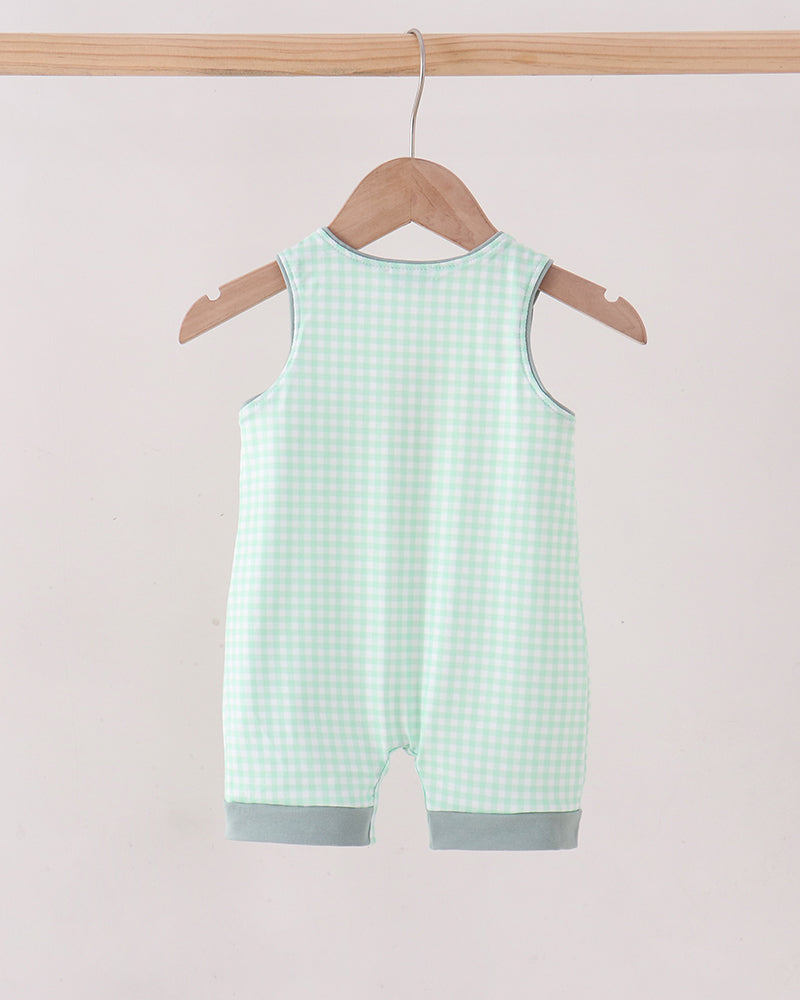 A sleeveless baby romper in a mint green and white gingham check pattern, hanging from a wooden hanger on a light wood clothing rack against a solid pale pink background.