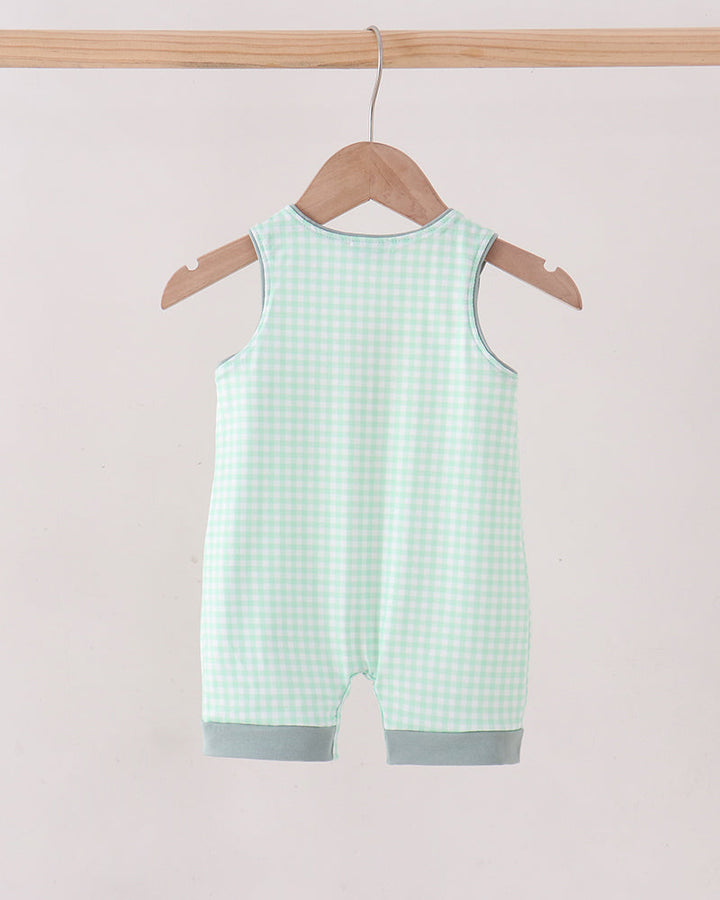 A sleeveless baby romper in a mint green and white gingham check pattern, hanging from a wooden hanger on a light wood clothing rack against a solid pale pink background.