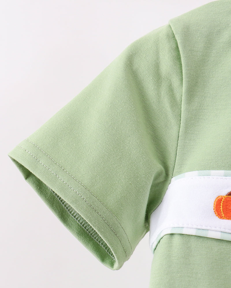 Close-up of a light green short-sleeve t-shirt featuring a white horizontal chest stripe with a small orange pumpkin graphic on the right side.