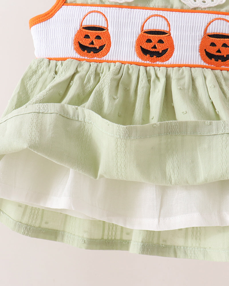 Close-up of a light sage green tiered dress with a white smocked waistband featuring three orange embroidered jack-o&