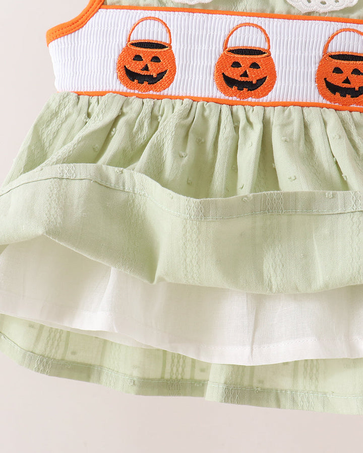 Close-up of a light sage green tiered dress with a white smocked waistband featuring three orange embroidered jack-o&
