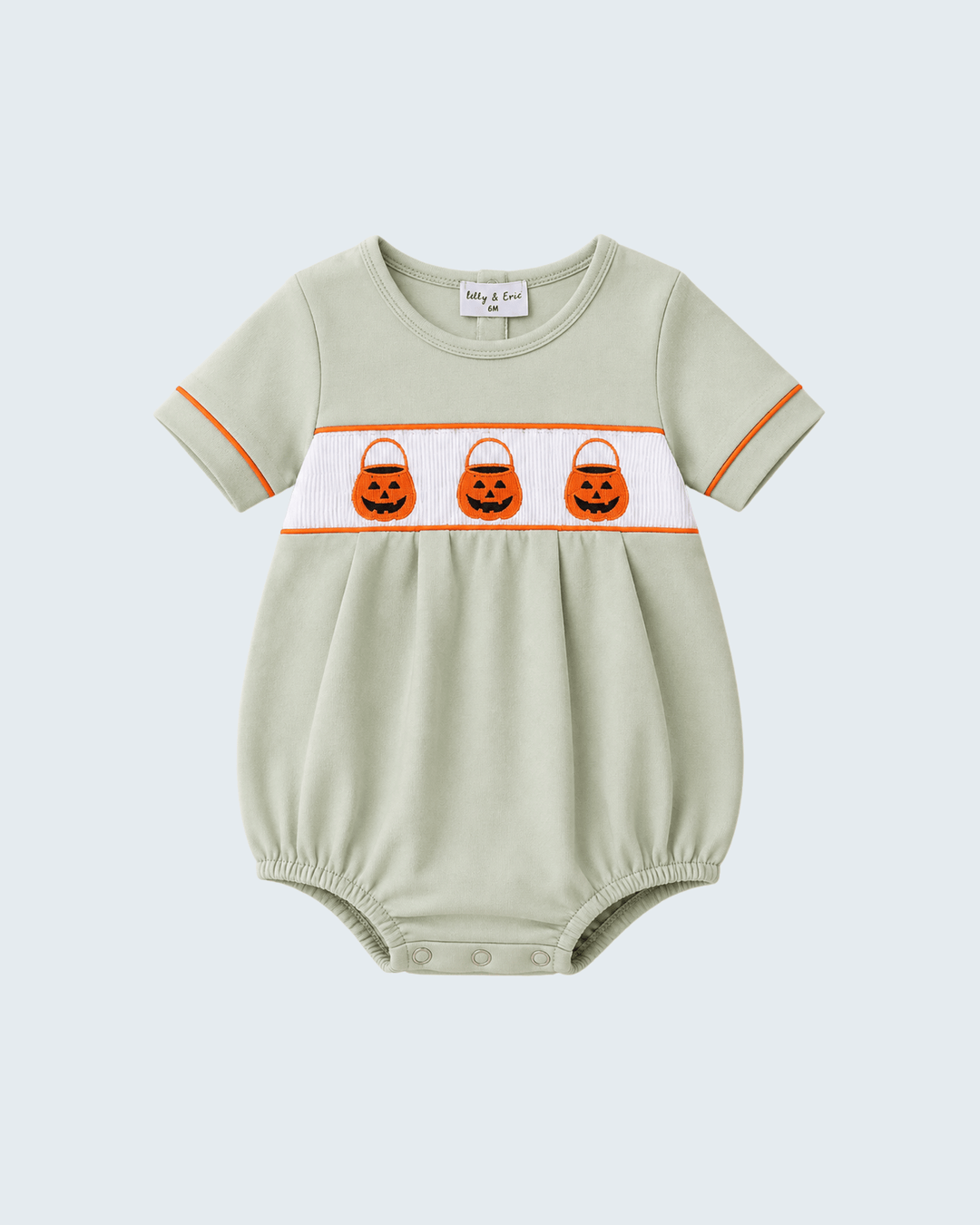 A baby short-sleeve romper in sage green with a white chest band featuring three embroidered orange pumpkin trick-or-treat bags, finished with orange piping on the sleeves, shown on a light gray background.