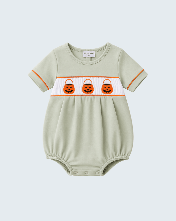 A baby short-sleeve romper in sage green with a white chest band featuring three embroidered orange pumpkin trick-or-treat bags, finished with orange piping on the sleeves, shown on a light gray background.