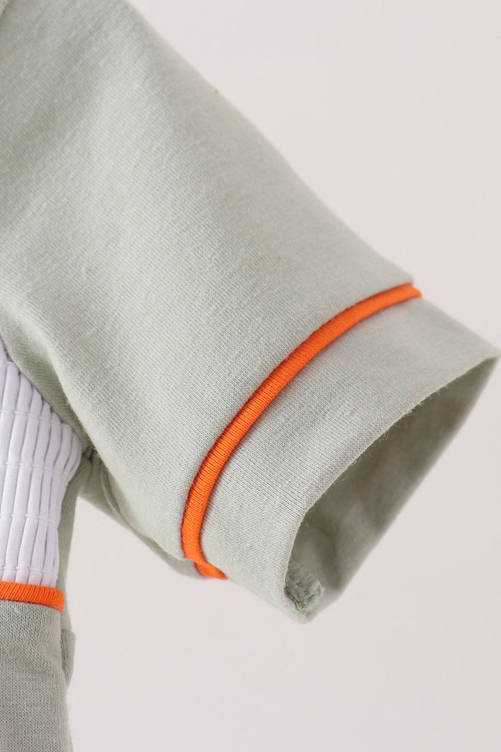 Close-up of a light sage green sleeve with bright orange piping trim and a white ribbed inner lining, shown against a plain light background.