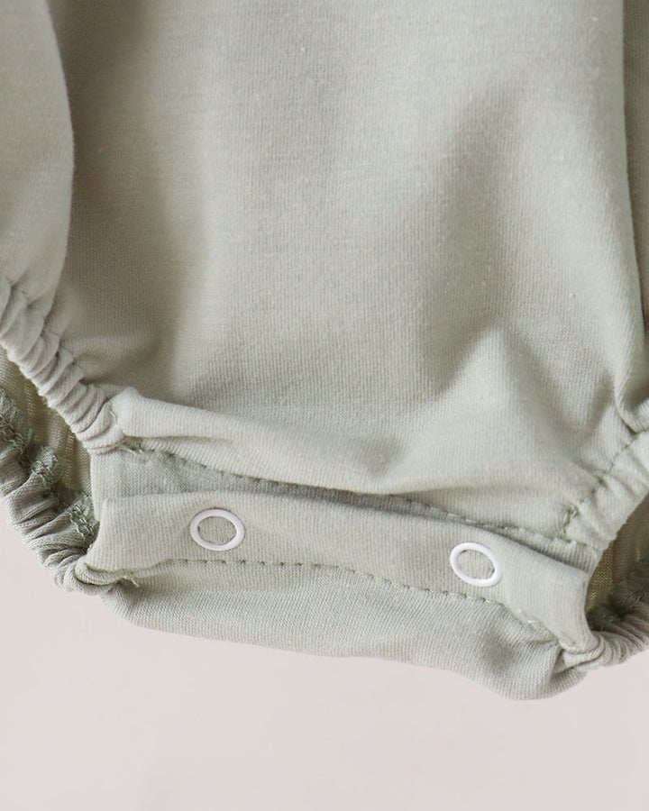 Close-up of a baby romper in a muted sage green color, showing the elasticized leg openings and two white snap buttons.