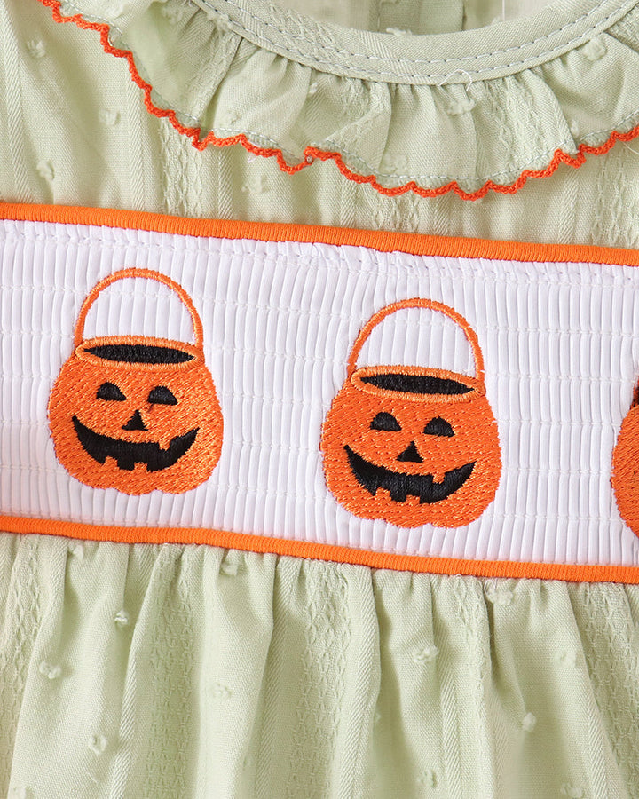 Close-up of a light sage green baby dress with orange trim, featuring a white smocked band decorated with embroidered orange jack-o&