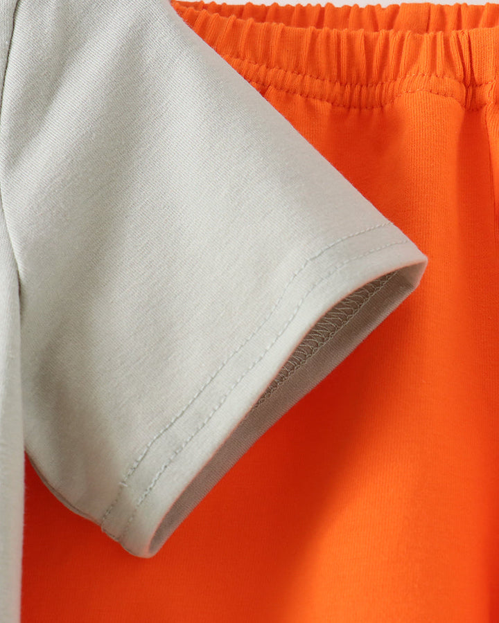 Close-up detail of a light sage green short-sleeve t-shirt sleeve with clean hem stitching, layered over bright orange shorts with an elastic waistband.