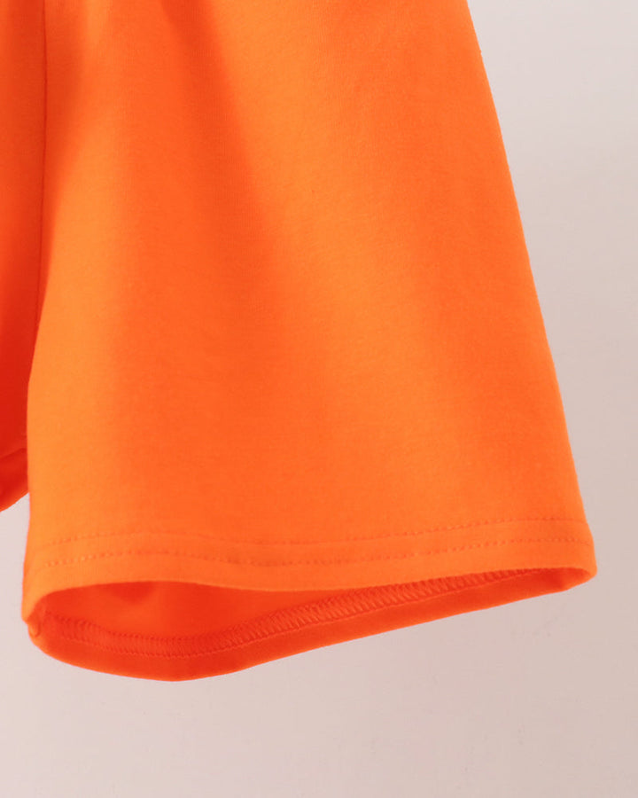 Close-up of a bright orange garment, showing the hem and folded edge of the sleeve against a plain light background.