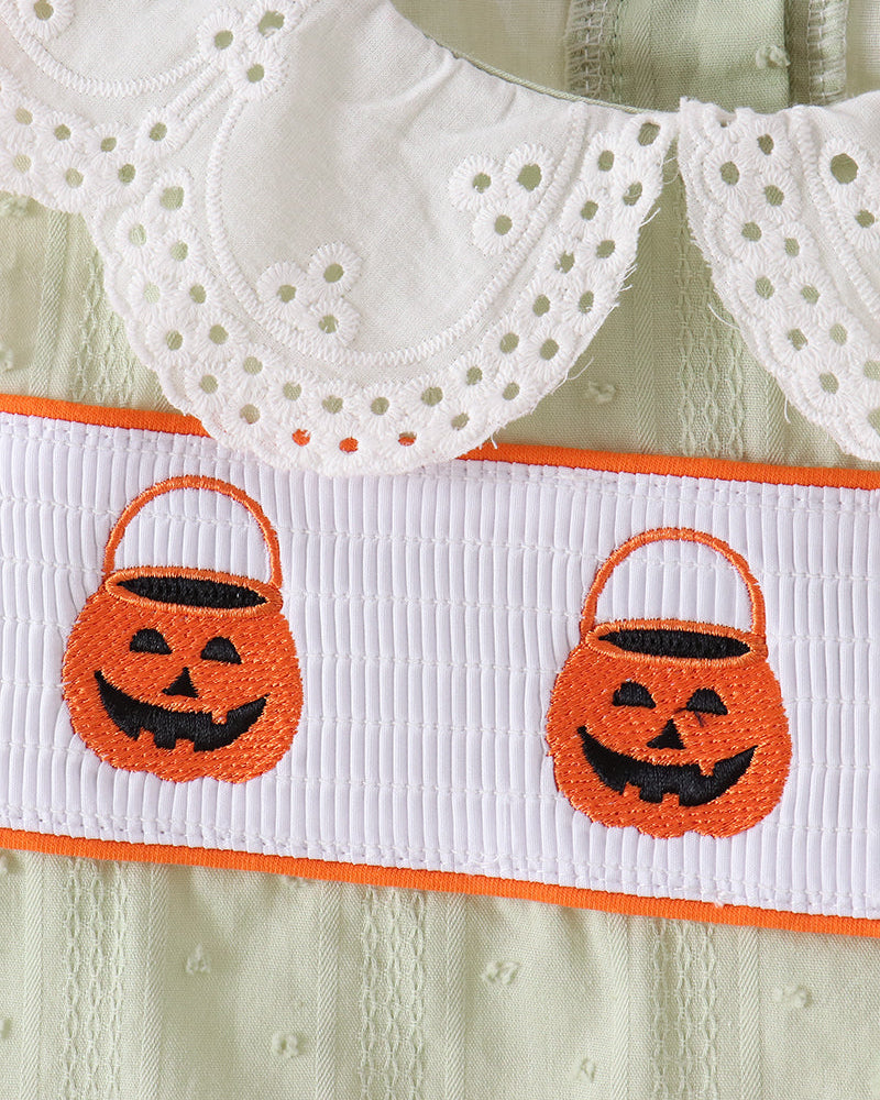 Close-up of a baby dress featuring a white eyelet Peter Pan collar, a white smocked bodice with orange trim, and two embroidered orange pumpkin bucket motifs on a decorative white band.