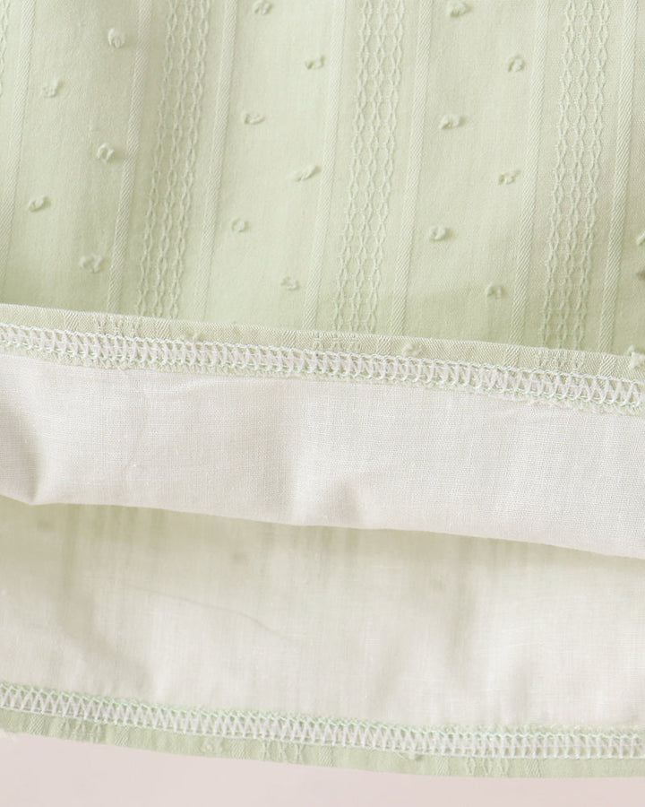 Close-up of a pale sage green embroidered fabric with vertical stitched details and a contrasting off-white hemmed edge.