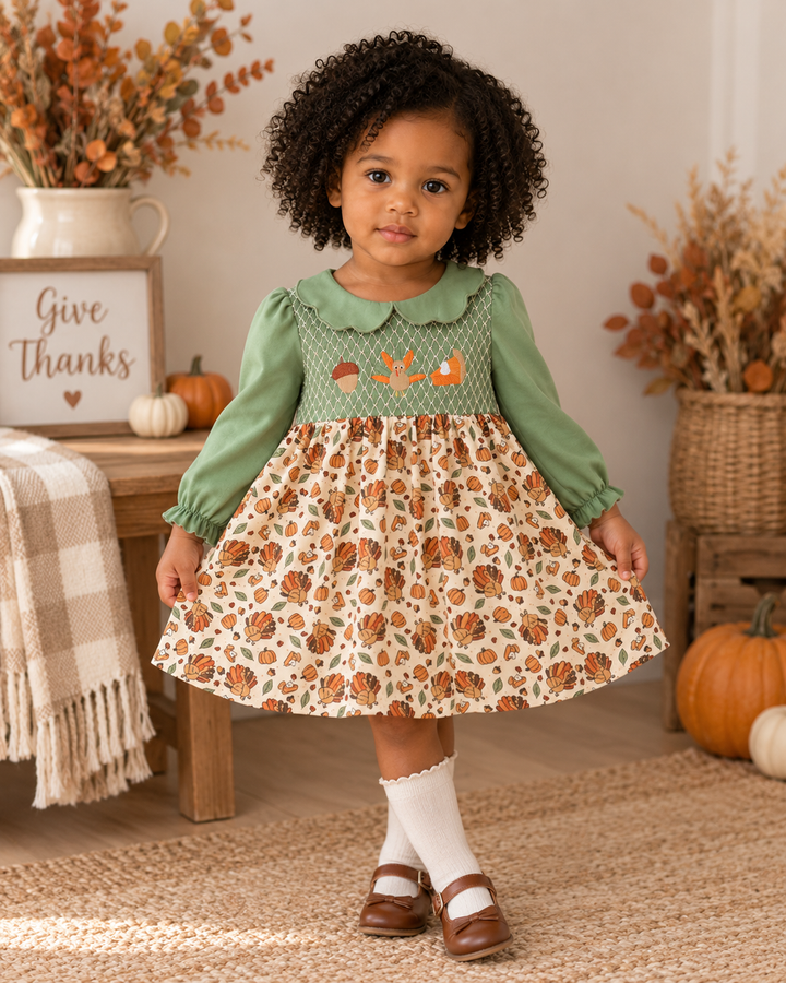 Green smocked dress with long sleeves, collar, and pumpkin/turkey print skirt