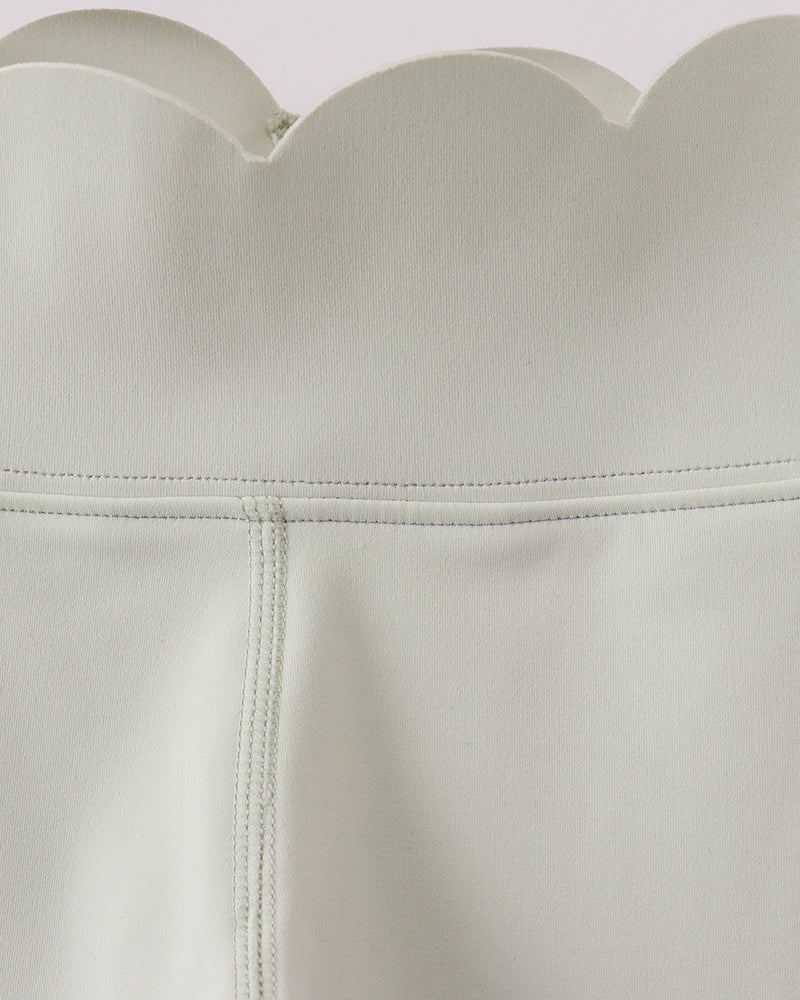 Close-up of a light green leggings with scalloped neckline and wooden object in the background.