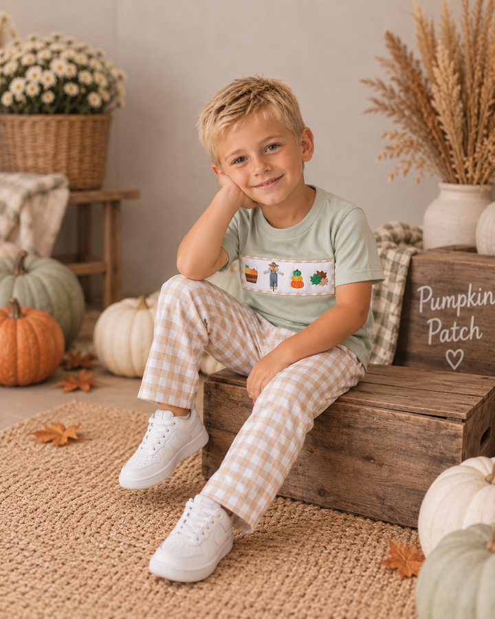 Young boy in beige gingham pants and fall shirt is sitting on a wooden box.