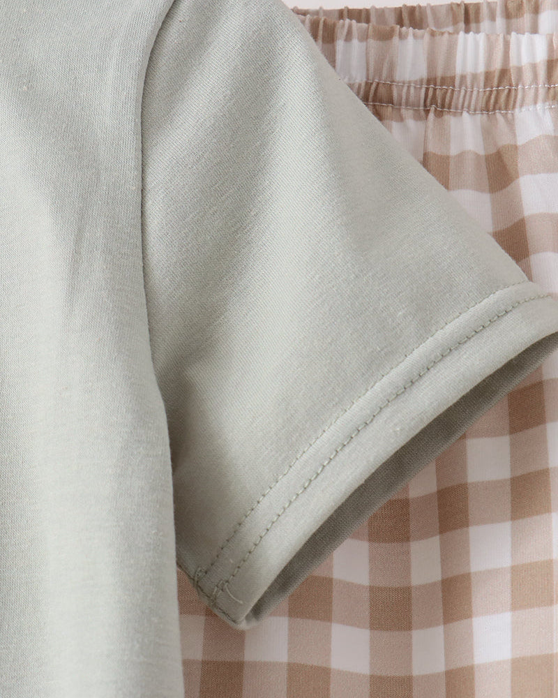 Close-up of a light sage green short-sleeve t-shirt sleeve, showing the fabric texture and hem, positioned in front of a beige and white gingham checkered skirt.