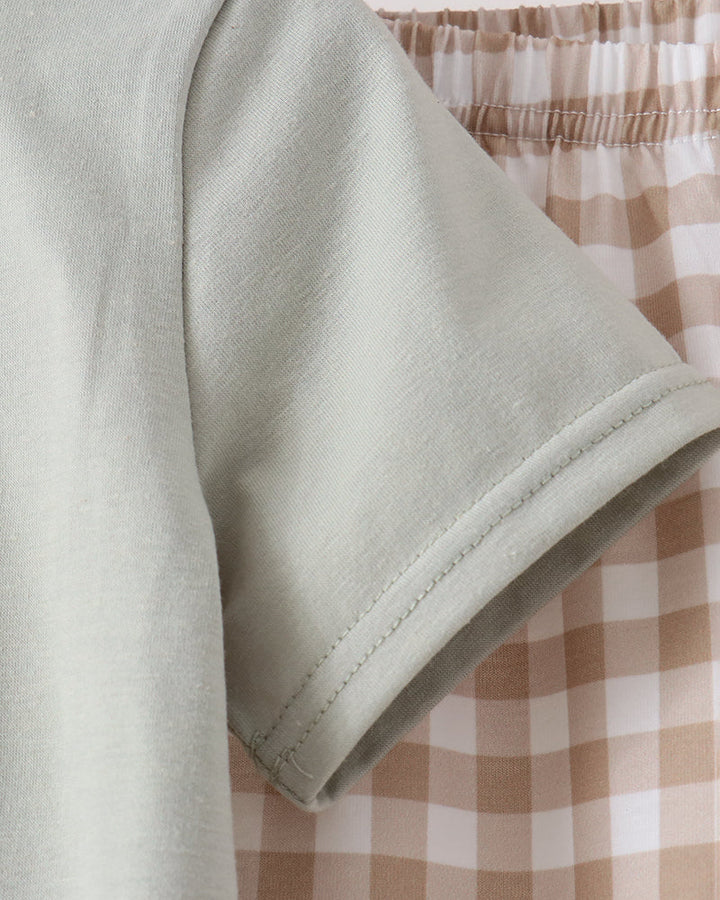 Close-up of a light sage green short-sleeve t-shirt sleeve, showing the fabric texture and hem, positioned in front of a beige and white gingham checkered skirt.