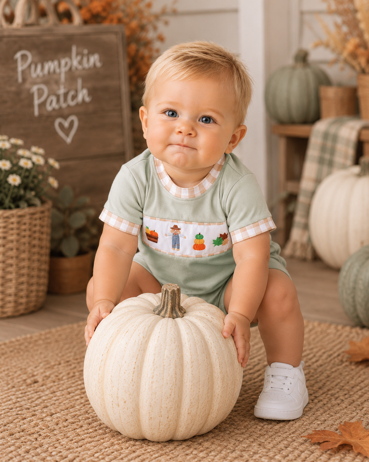 Baby boy is a cute fall romper is trying to lift a heavy pumpkin.