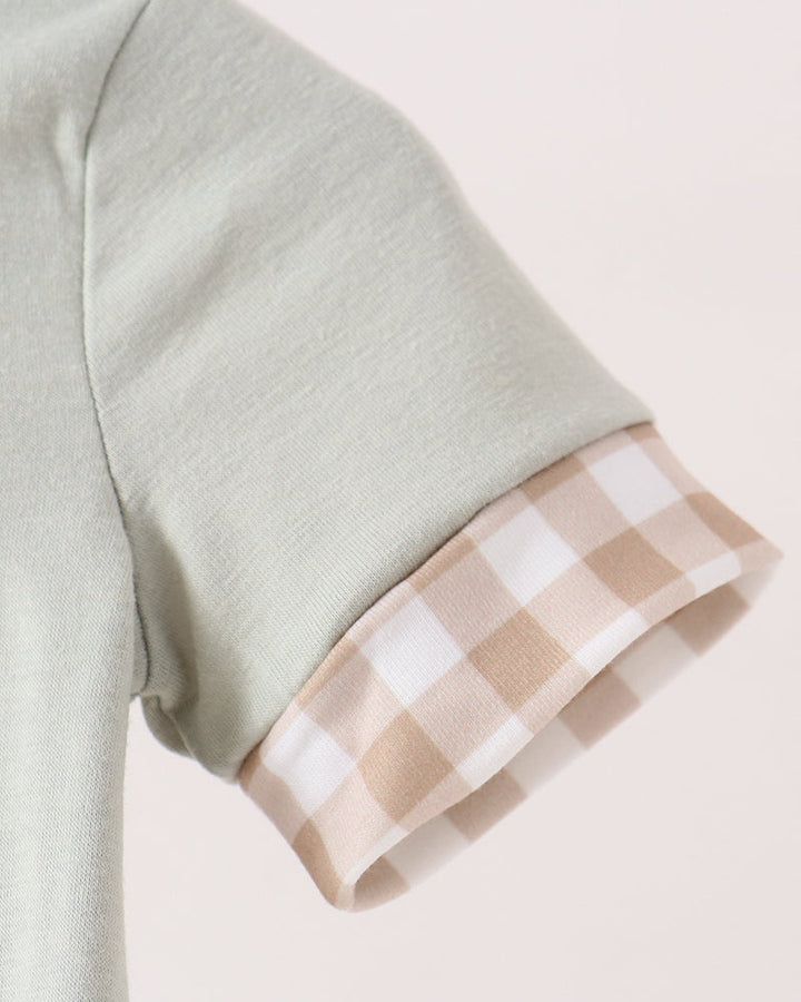 Close-up of a short-sleeve top showing a sage green main fabric and a beige and white gingham checkered cuff.