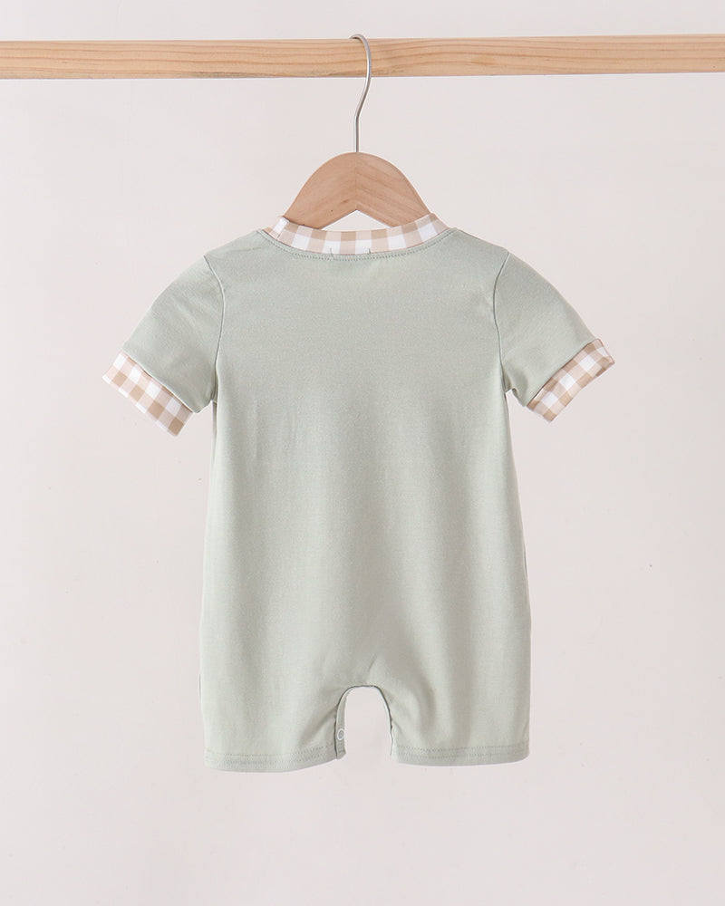 A baby short-sleeve romper in pale sage green, hanging on a wooden hanger from a light wood rod. The romper features a beige and white gingham patterned collar and sleeve cuffs, shown against a plain off-white background.