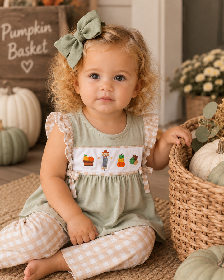 Toddler girl in a cute fall inspired outfit, sitting by a basket of pumpkins.