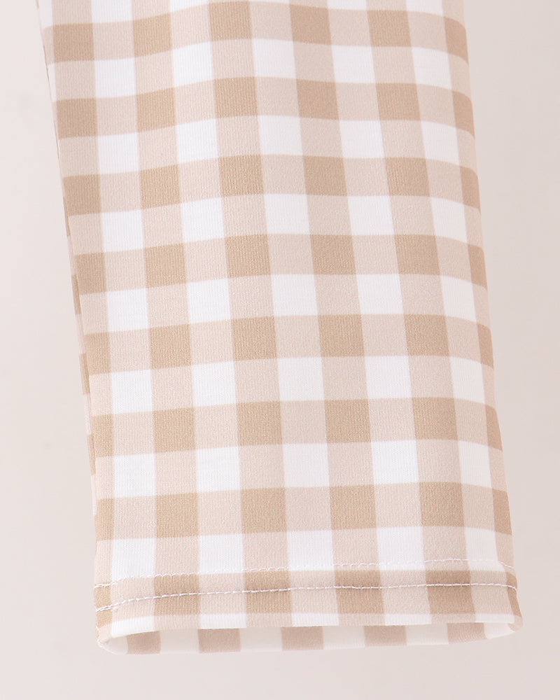 A close-up of a beige and white gingham checkered fabric, likely a tablecloth or napkin, folded neatly on a light cream background.