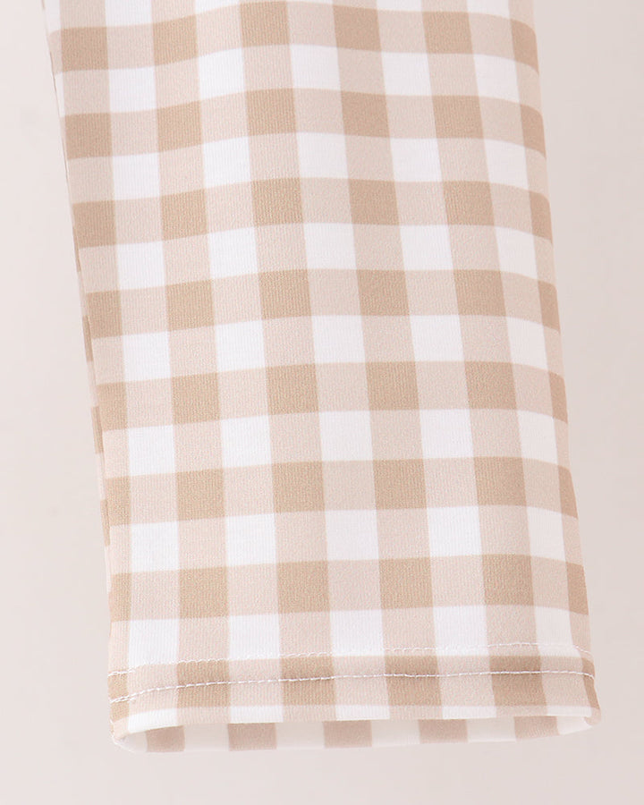A close-up of a beige and white gingham checkered fabric, likely a tablecloth or napkin, folded neatly on a light cream background.