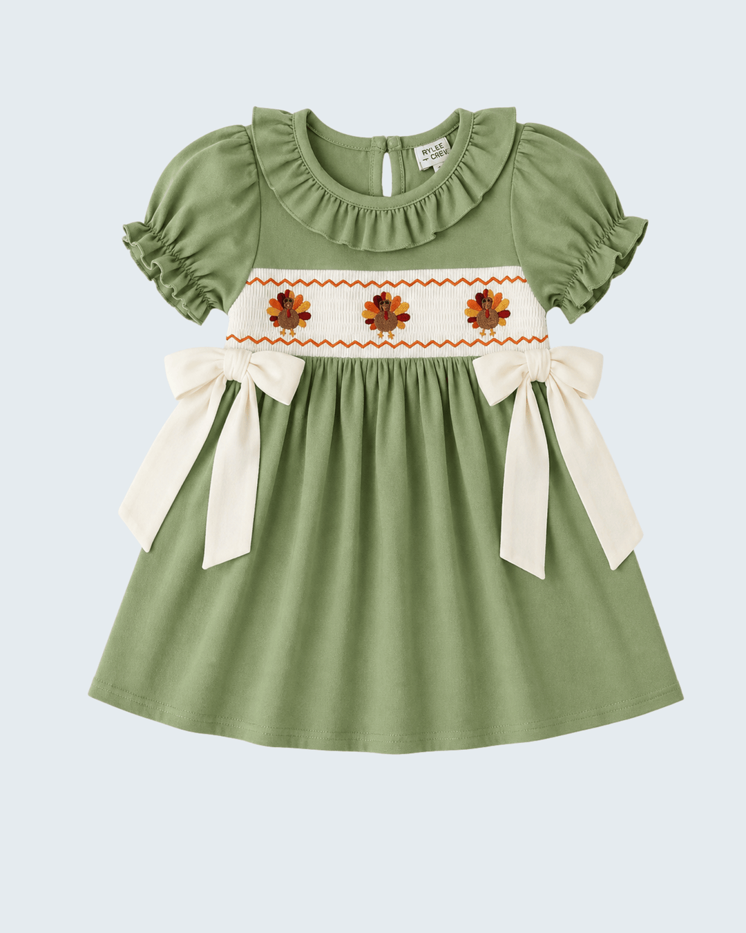 Green embroidered smock dress with white yoke flowers, orange trim, and ribbon bows.