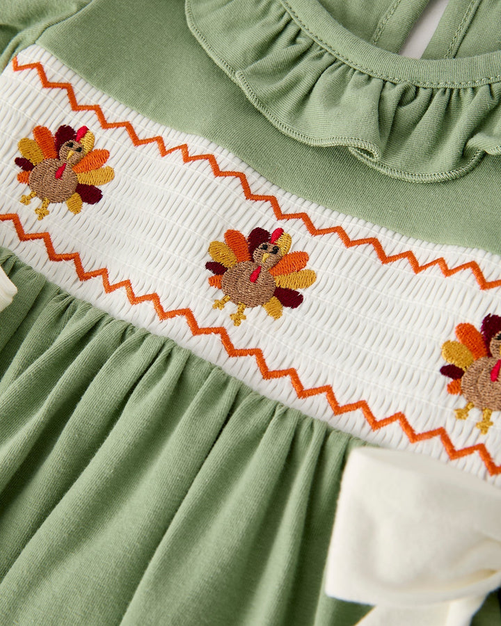 Green smock dress with white yoke panel and orange-stitched flower embroidery.