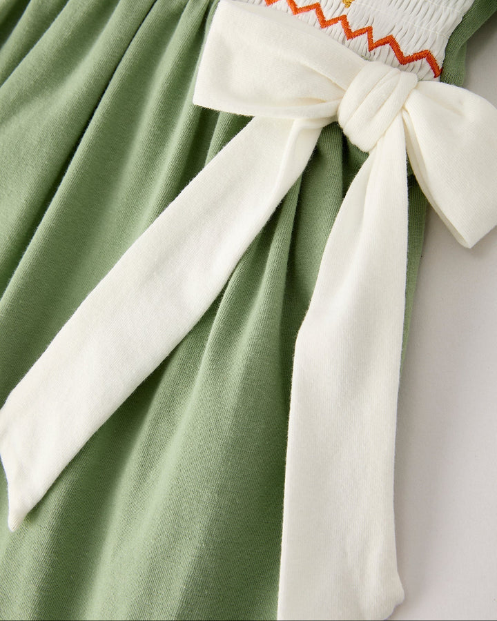 Green smock dress with white bow-tied waist detail and gathered skirt.