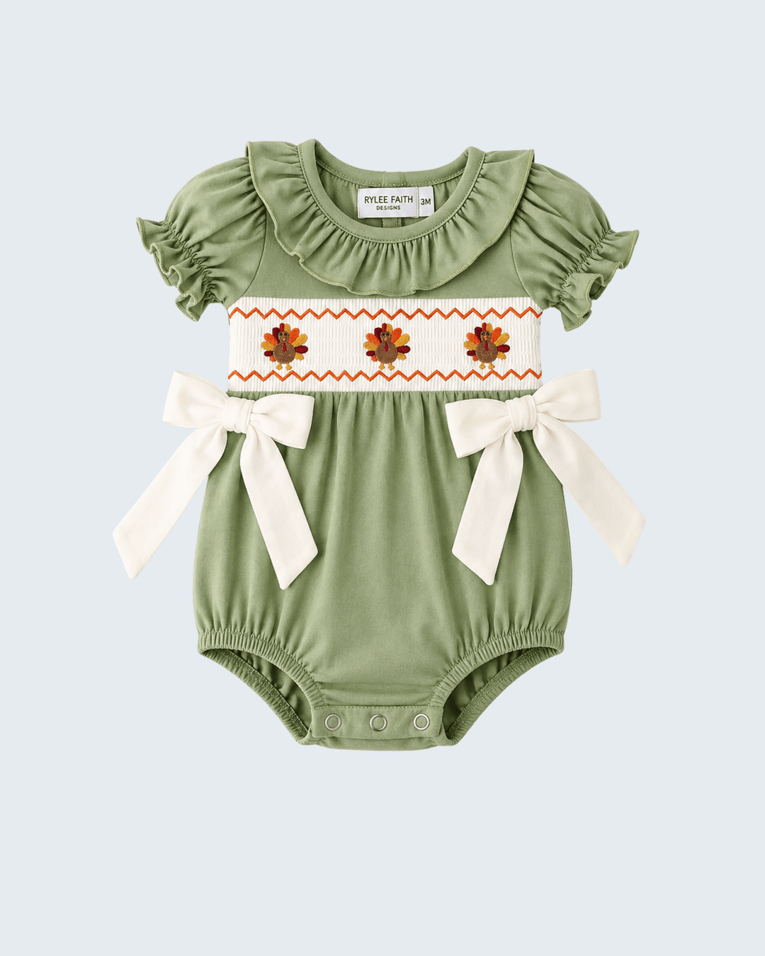 Green embroidered romper with white panel, orange flowers, and bow ties