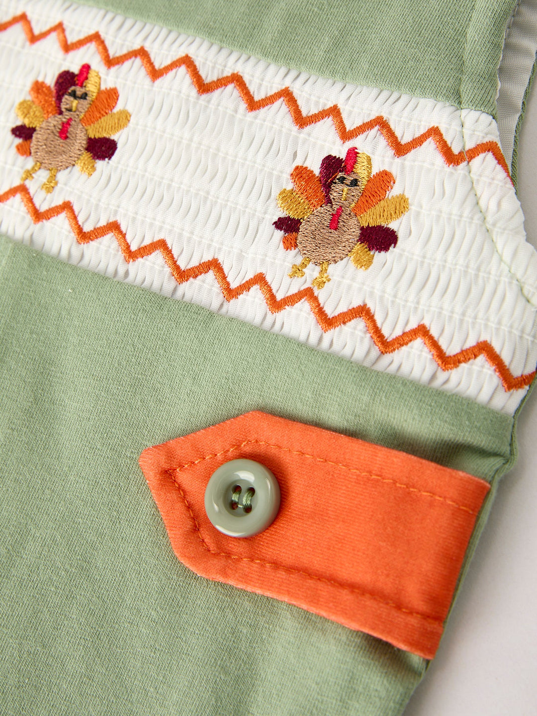 Embroidered yoke on green romper with floral motifs and orange zigzag trim