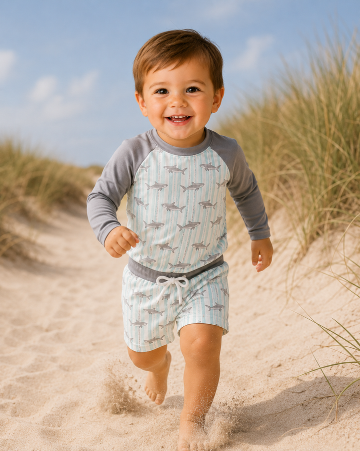 Child running on a sandy beach wearing a patterned shirt and shorts.