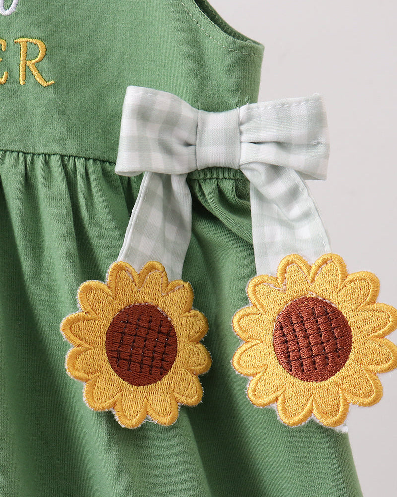 Green dress detail with white bow and sunflower applique patches at waist