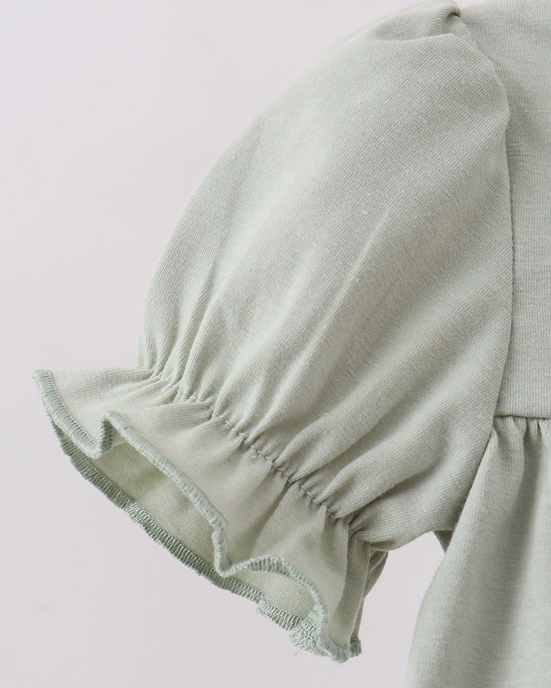 Close-up of a light sage green garment featuring a gathered puff sleeve with a ruffled hem and a matching solid fabric body.