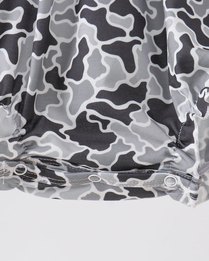 Close-up of a gray and black abstract camouflage-patterned fabric with a gathered hem and snap buttons, set against a light gray background.