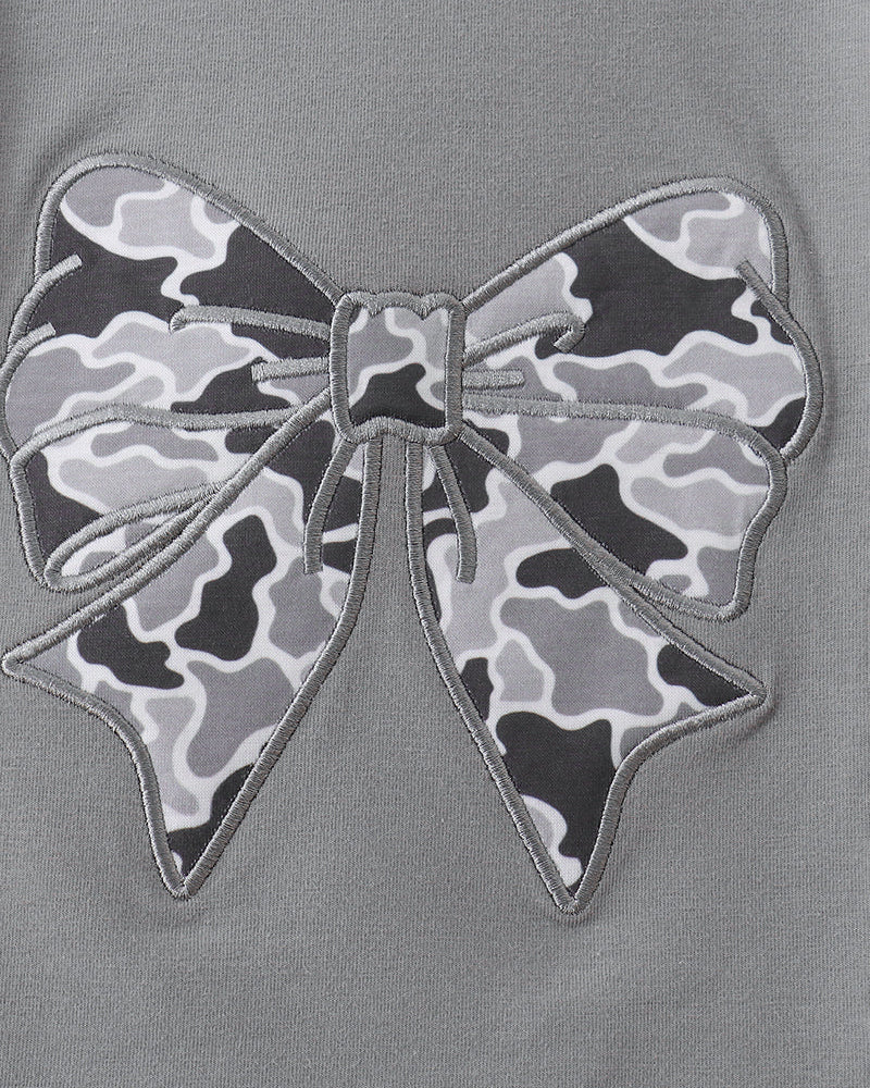 Close-up of a gray top featuring a large bow applique with a black, gray, and white camouflage pattern and gray embroidered outline.