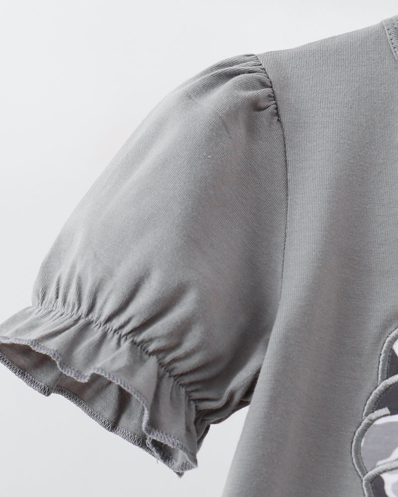 Close-up of a light gray short-sleeve top with gathered puff sleeves and a ruffled hem, showing part of a tonal graphic on the lower right.