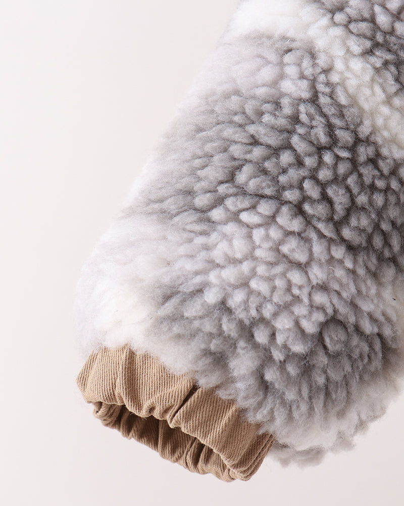 Close-up of a soft, textured gray and white faux fur or sheepskin sleeve with a tan ribbed cuff, shown against a plain off-white background.