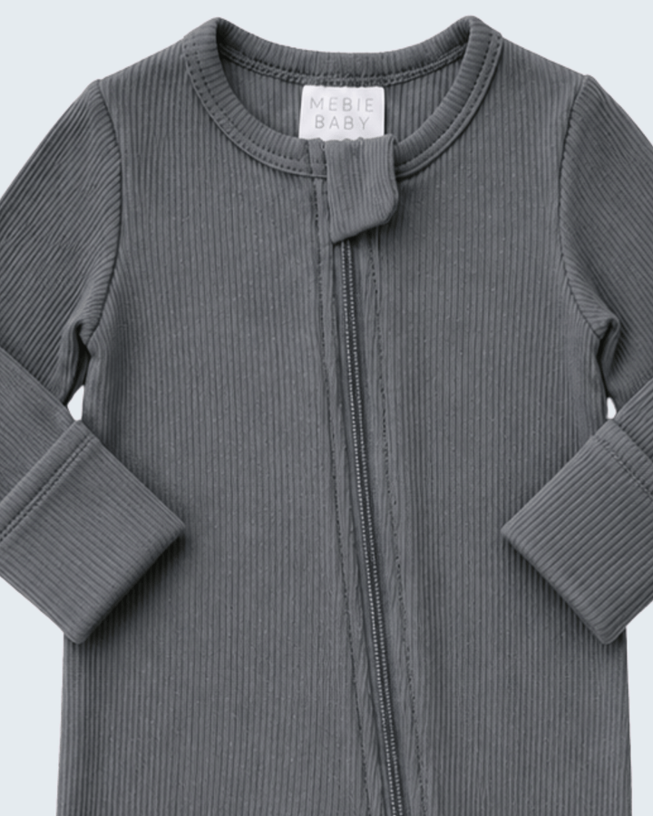 A close-up of a dark gray ribbed long-sleeve baby zip-up garment with a small fabric tie detail at the neckline. A white neck label reads &